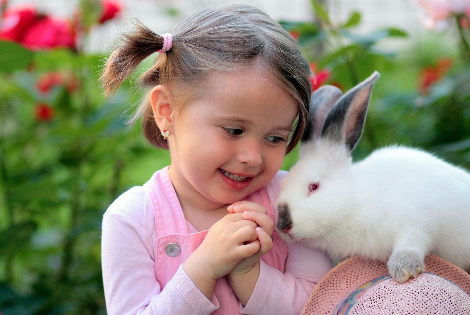 Jong meisje knuffelt een wit konijn in de tuin